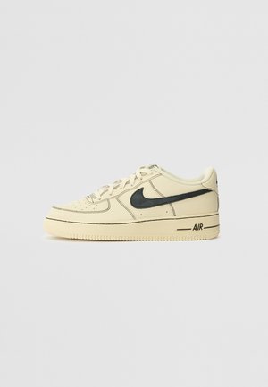 Off-white Nike Air Force 1 matalavartinen lenkkari, jossa musta swoosh-logo ja "AIR"-teksti pohjassa, nähtynä sivulta yksinkertaisella taustalla.