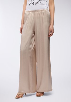 Pantaloni larghi e leggeri in satin beige chiaro con una sottile lucentezza e vita elastica. Abbinati a una maglietta bianca con testo nero.