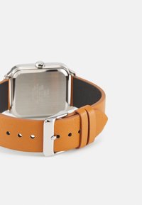 Montre carrée avec un boîtier en métal argenté, bracelet en cuir orange avec des trous et une boucle en métal poli. Le dos est en acier inoxydable.