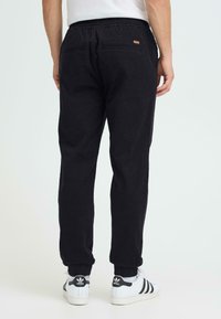 Joggers noirs en coton avec une taille élastique, des chevilles resserrées et deux poches arrière. Associés à des baskets blanches avec des accents noirs.