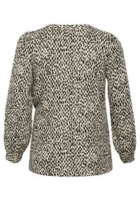 Blus med långa ärmar i krämfärg med ett mönster av svarta oregelbundna prickar, med rund halsringning och något puffiga ärmar.