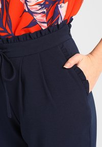 Námořnické modré kalhoty vyrobené z hladké látky, s volánkovým pasem, elastickým stahováním, bočními kapsami a přiléhavým střihem.