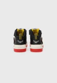 Black high-top sneakers with yellow accents, red rubber soles, reinforced heel, and velcro strap. Features logo on the back and vertical stripes.