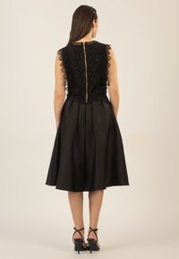 Vestido negro con un corsé de encaje y bordes festoneados, cintura entallada y falda acampanada. Cierre de cremallera en la parte posterior. Sandalias de tacón negras.