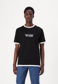 Black t-shirt with short sleeves, white ribbed collar and cuffs, featuring white stylized text on the front. Cotton material, relaxed fit.