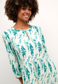 Rochie florală cu un material alb și modele florale turcoaz, mâneci 3/4, decolteu în formă de cheie și fustă evazată.
