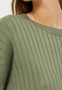 Pull surdimensionné en vert clair avec un col large, présentant des rayures verticales et un tissu texturé pour une dimension ajoutée.