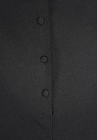 Černá látka košile s hladkým povrchem a pěti viditelnými knoflíky vpředu, z nichž každý je kulatý a má prošívané detaily.