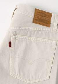Gros plan sur la poche d'un jean en denim de couleur crème avec l'étiquette rouge Levi's et un patch en cuir marron Levi Strauss & Co. au-dessus de la ceinture.