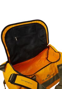 Quiksilver-käsilaukku, keltainen ulkopinta mustilla yksityiskohdilla, suuri avaus, sisällä verkkotasku ja säädettävät hihnat.
