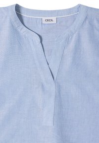 Chemise en lin bleu clair avec un col fendu en V et une étiquette de marque visible "CECIL" à l'intérieur du col.