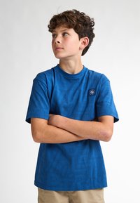 Tričko s krátkým rukávem modré barvy, které má texturovaný vzor písmen a kulatý výstřih. Obsahuje malou logovou nášivku na hrudníku.