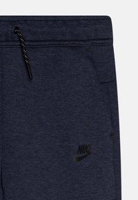 Tumši zili treniņbikses ar teksturētu apdari, ar melnu Nike logo un regulējamu auklu ar melnu aparatūru.