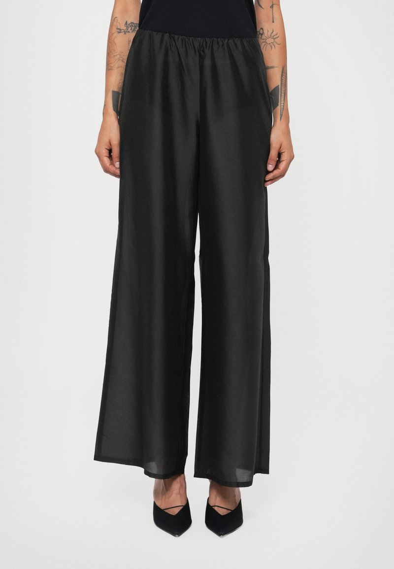 Black wide-leg pants made of soft fabric with a smooth texture and elastic waistband. Paired with pointed black heels.