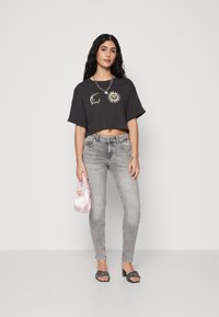 Svart avkortet t-skjorte med sol- og måneddesign, kombinert med lysegrå skinnyjeans. Tilbehøret inkluderer en rosa veske og svarte hælesandaler.