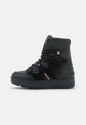 Black high-top sneaker with thick sole, padded ankle, lace-up front, and red, white, and blue stripe accents on side and branding on sole.
