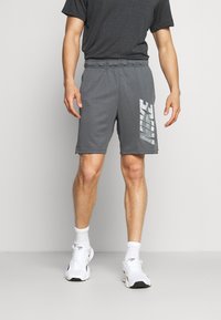 Graue Sportshorts aus weichem Material, mit einem elastischen Bund und einem großen weißen Nike-Logo, das auf der linken Seite gedruckt ist.