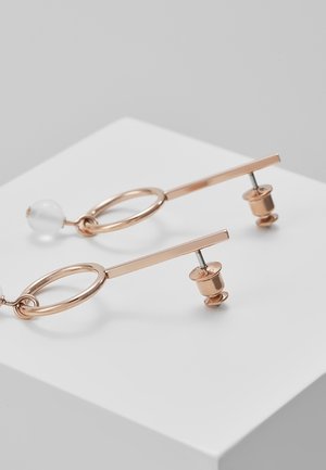 Roze gouden hangende oorbellen met een ontwerp van een staaf en een ovale lus, elk met een klein doorschijnend kraaltje aan het uiteinde, getoond op een witte ondergrond.