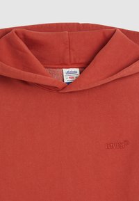 Červená mikina s kapucňou, vyrobená z mäkkého bavlneného materiálu. Má vyšitý logo Levi's na prednej strane a uvoľnený strih.