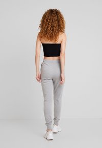 Grå mjukisbyxor med elastiska muddar och fickor i sidorna, kombinerade med en svart axelbandslös topp. Modellen vänder ryggen mot kameran med lockigt hår.