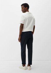 Witte kortebloem t-shirt gecombineerd met donkerblauwe broek. Model draagt crèmekleurige sneakers. Minimalistisch ontwerp met eenvoudige lijnen en zonder patronen.