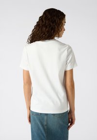 T-shirt en coton blanc à manches courtes, col rond et design épuré. La vue de dos révèle une texture de tissu lisse sans motifs ni accents.