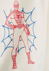 Červený obrys Spider-Mana s motívmi pavučiny stojí s jednou rukou na boku na modrom pavučinovom vzore na bielom textilnom pozadí.