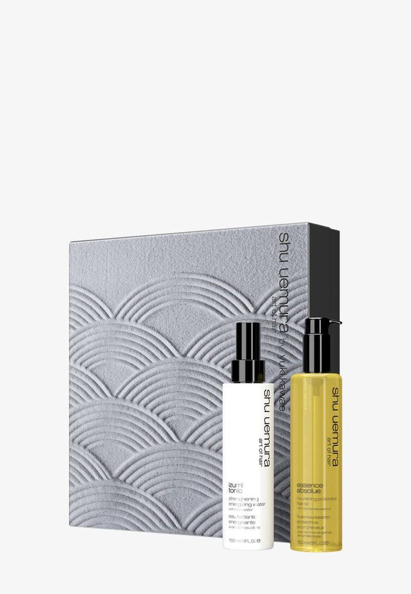 Grå presentlåda med vågmönster, innehållande en vit flaska med svart pump märkt "izumi tonic" och en gul flaska med svart pump märkt "essence absolue."