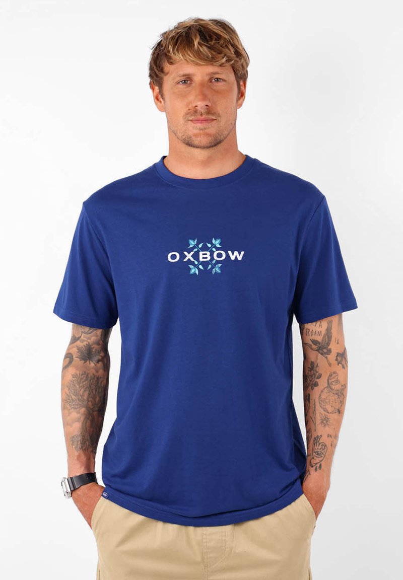 T-shirt en coton bleu marine avec un logo "OXBOW" blanc et turquoise, manches courtes et coupe décontractée. Texture lisse avec un design casual.