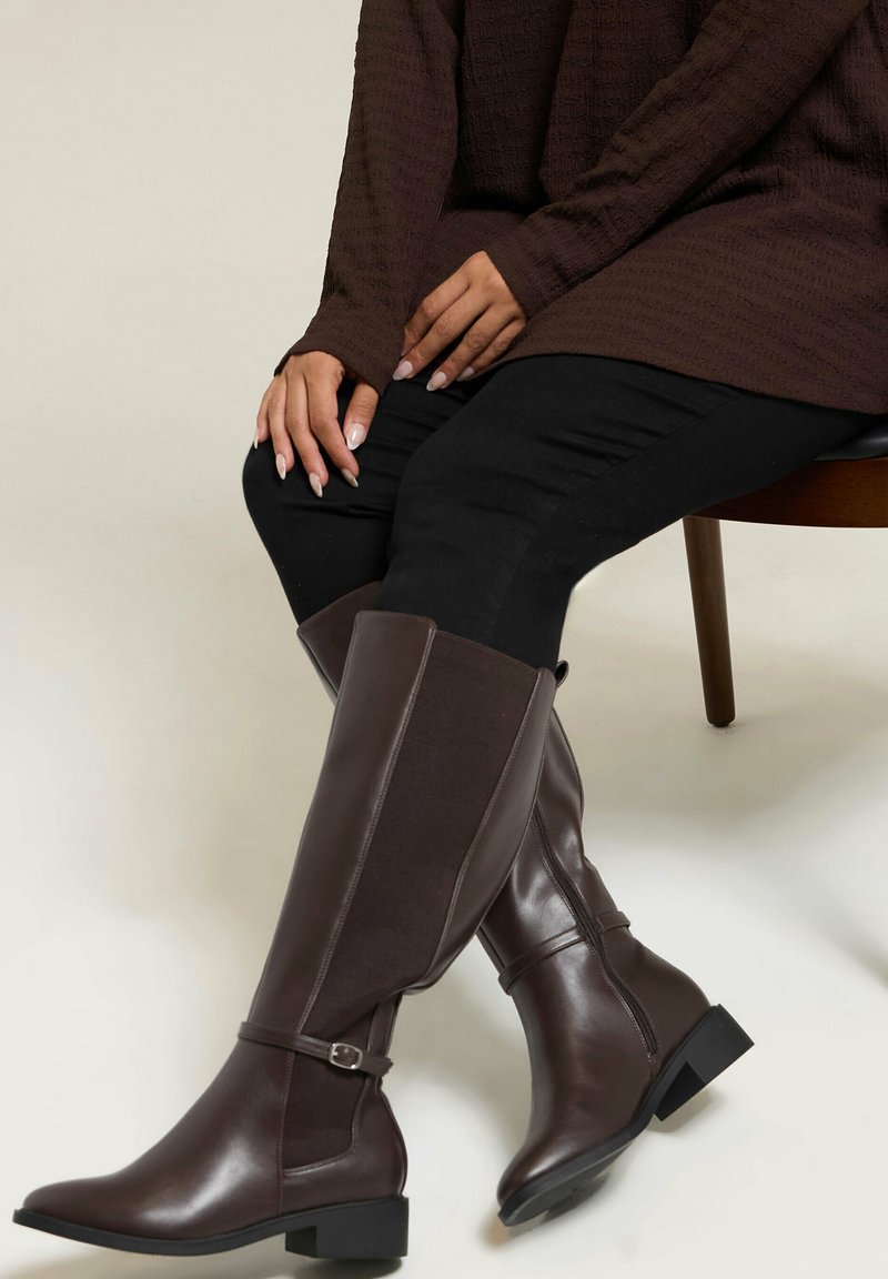 Kozaki do kolan w kolorze brązowym, łączące gładką skórę i teksturowany materiał, z paskiem na kostce, niskim słupkowym obcasem i zaokrąglonym noskiem.