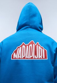 Blauwe hoodie met een wit en rood bergvormig logo en de tekst "NAPAPIJRI" op de achterkant. Zacht materiaal met een gestructureerde afwerking.