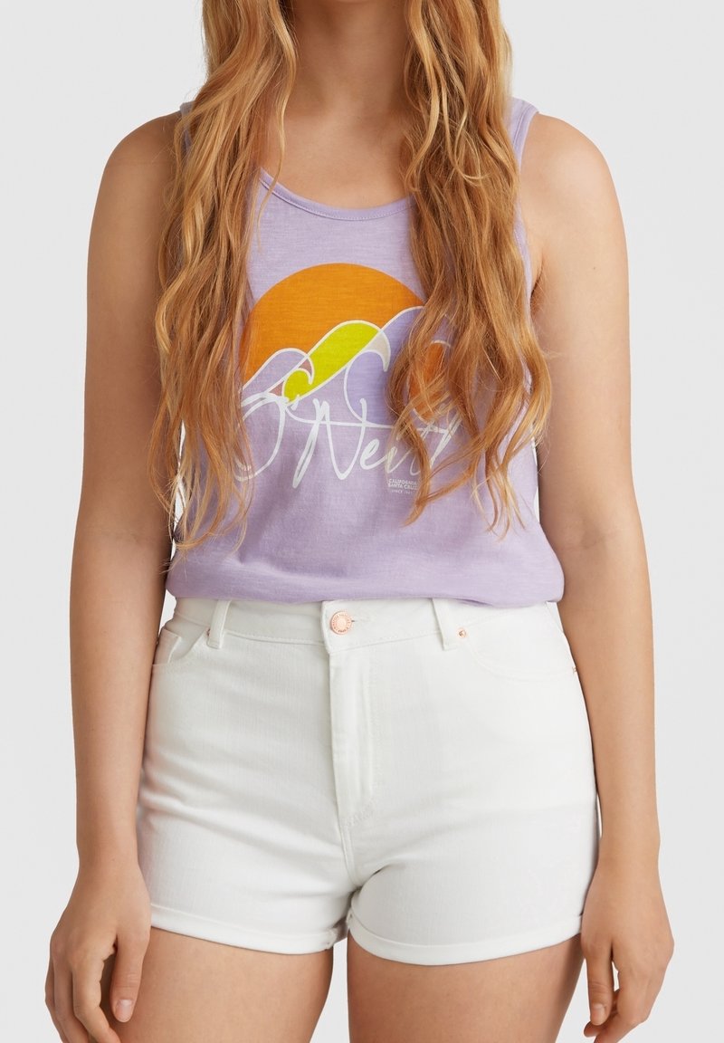 Femme aux longs cheveux ondulés, portant un débardeur violet avec un motif coucher de soleil et vagues, et un short blanc taille haute sur un fond uni.