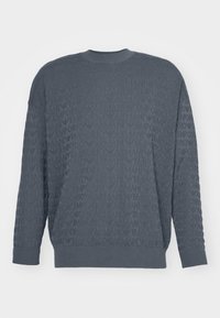 Szara bluza z teksturowanym wzorem z logo na całej powierzchni, z okrągłym dekoltem, długimi rękawami, ściągaczami na mankietach i u dołu. Miękki materiał o luźnym kroju.