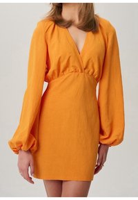Oranžové lněné mini šaty s dlouhými balónovými rukávy, hlubokým výstřihem do V a nařaseným pasem pro přiléhavý siluetu. Hladká textura, minimální detaily.