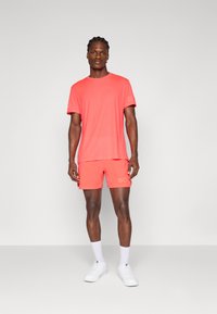 Coral athletic t-shirt and shorts set. Short sleeves, crew neck, and 'B' logo on shorts. Smooth, lightweight fabric with a relaxed fit.