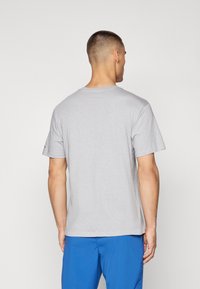 Camiseta de algodón gris con cuello redondo y mangas cortas. Presenta un corte relajado, textura suave y un diseño minimalista.
