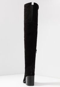 Botas negras de ante por encima de la rodilla con tacón cuadrado, con un detalle de costura y una cremallera en la parte trasera para facilitar su uso.