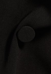 Čern�á látka s jemnou texturou, na které je přišitý malý kulatý černý knoflík. Látka vypadá hladce a je jemně tkaná.