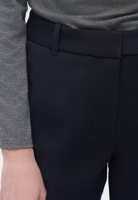 Marinblå byxor med en slät textur, utrustade med en bred midja och sidofickor. Tillsammans med en åtsittande grå långärmad topp.