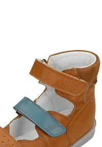 Hnědé kožené boty s modrým suchým zipem, otevřenými stranami a měkkým bílým vnitřkem. Má šité akcenty a gumovou podrážku.