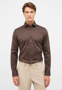 Braune, knöpfbare Hemd mit einem dezenten Muster, langen Ärmeln und einem klassischen Kragen. Kombiniert mit hellbeigen Hosen, ergibt es einen eleganten Look.