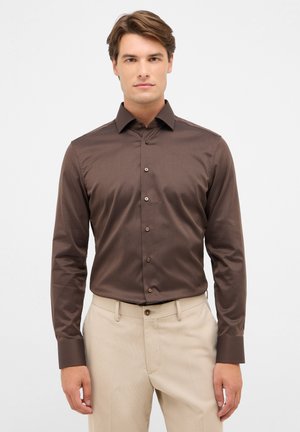 Camicia button-up marrone con un motivo sottile, maniche lunghe e colletto classico. Abbinata a pantaloni beige chiaro, creando un look curato.