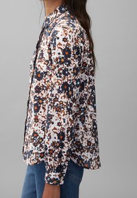 Camicia a bottoni floreale in tessuto leggero. Presenta una combinazione di colori blu navy, arancione e bianco, con maniche lunghe e colletto classico.