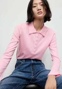Rosa Langarm-Polohemd mit Kragen, ausgestattet mit einer Knopfleiste. Kombiniert mit hoch geschnittenen Jeans aus Denim, die eine lockere Passform zeigen.