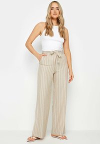Lichtbeige wijde broek met verticale witte strepen, hoge taille en strikdetail. Het materiaal lijkt zacht en comfortabel te zijn met zijzakken.