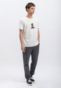 Witte katoenen t-shirt met een kleurrijk grafisch ontwerp op de borst, gecombineerd met grijze broek met elastische taille en subtiele stikselaccenten.