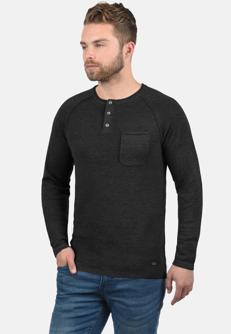 Tamno siva long-sleeve henley majica s teksturiranim materijalom, placketom s tri gumba i džepom na prsima. Uparena s plavim trapericama.