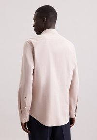 Camicia a maniche lunghe rosa chiaro in tessuto testurizzato, con colletto a punta, polsini con bottone e orlo curvo.
