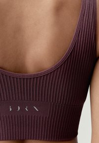 Sujeción deportiva de rayas en color burdeos con un amplio escote en la espalda y una banda texturizada que presenta un sutil logo en la parte delantera. Material suave y elástico.
