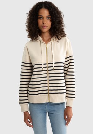 Felpa con zip di colore crema, con strisce orizzontali nere, cappuccio con cordini e polsini a costine. Tessuto morbido con dettagli in zip dorati.